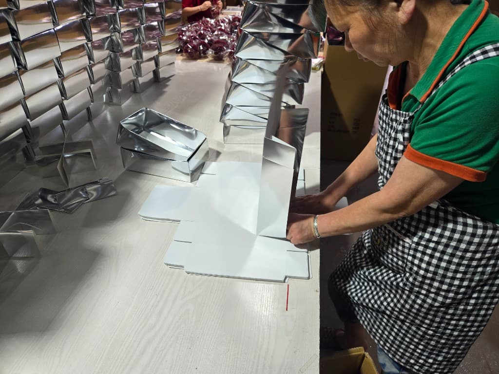Factory worker assembling silver retail gift boxes for Christmas wreath and ornament export programs